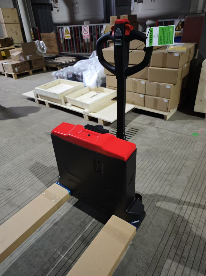 CBD20W-II electric pallet jack photographed from the fork end at a raised angle, showing the red battery cover, black battery housing and tiller handle with the forks in protective wrap